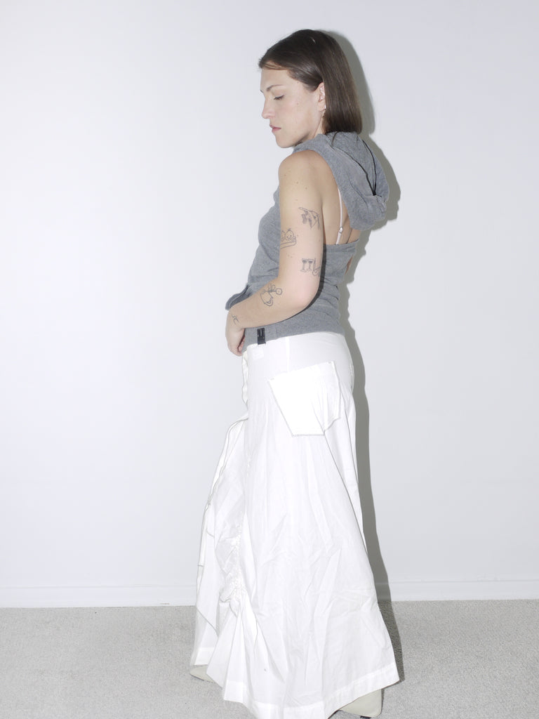 Sporty grey sleeveless hoodie with button placket, paired with a voluminous white ruched maxi skirt and white pointed knee-high boots—blending casual comfort with dramatic silhouette.