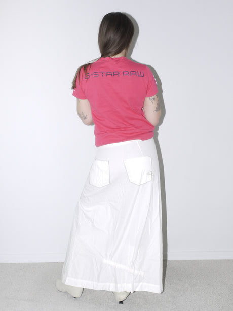 Back view of a vintage G-Star Raw logo tee in bold pink, paired with a white maxi skirt featuring large back pockets and ruching details, styled with cream pointed boots for a bold casual look.