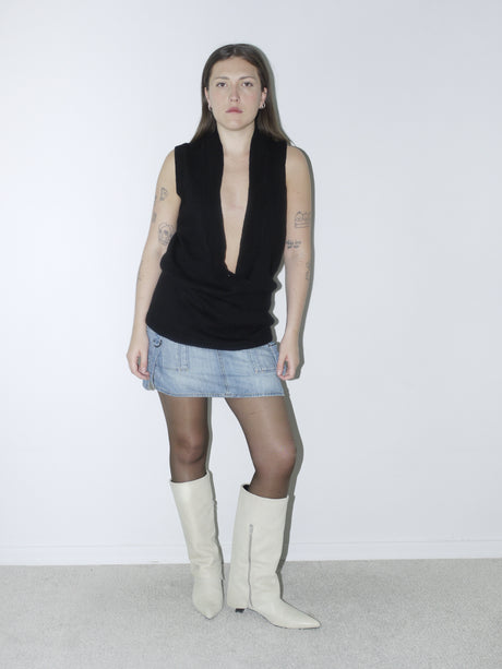 Original Maison Margiela black sleeveless pullover with deep plunging neckline, styled with a low-rise denim mini skirt and cream pointed boots – bold and minimalist archival look.
