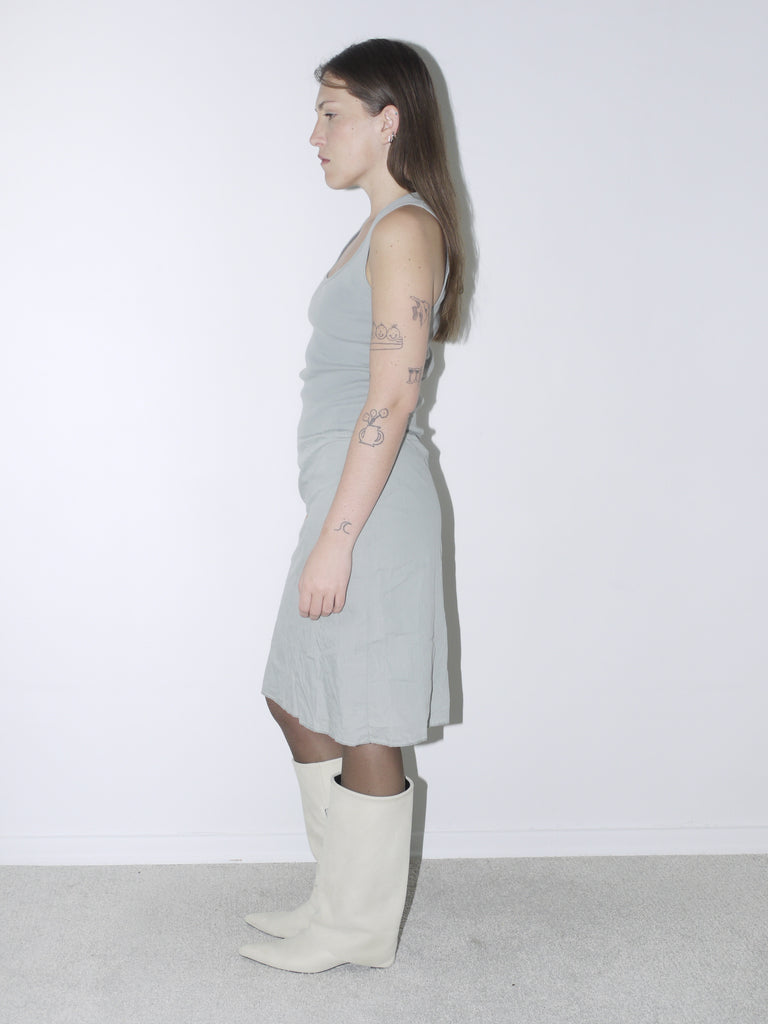 Original Maison Margiela minimalist dress in soft sage green with a fitted tank silhouette, worn with cream pointed boots – understated and architectural, perfect for a quiet luxury statement.