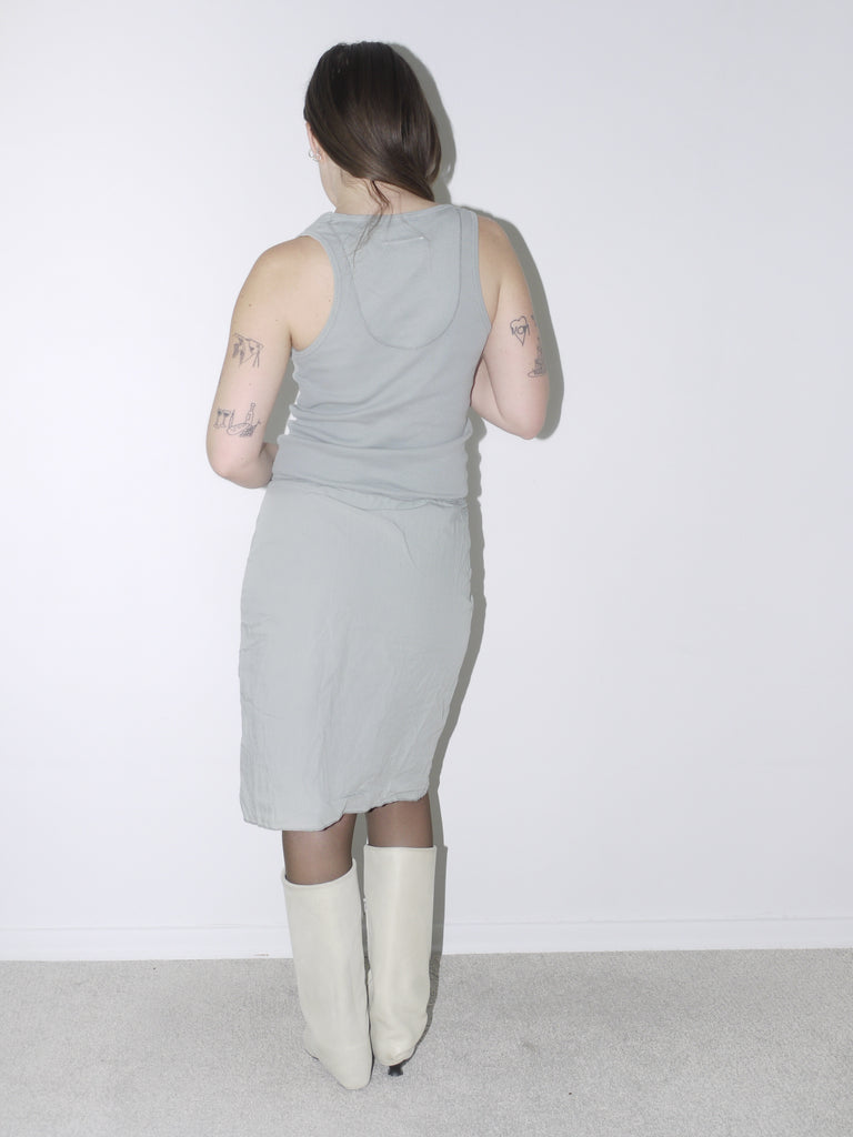 Original Maison Margiela minimalist dress in soft sage green with a fitted tank silhouette, worn with cream pointed boots – understated and architectural, perfect for a quiet luxury statement.