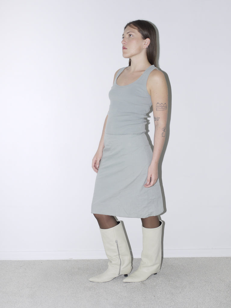 Original Maison Margiela minimalist dress in soft sage green with a fitted tank silhouette, worn with cream pointed boots – understated and architectural, perfect for a quiet luxury statement.