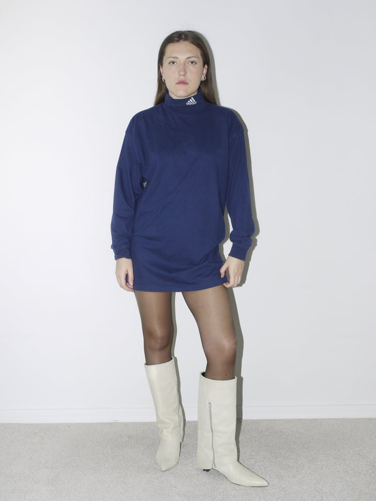 Vintage navy blue Adidas long-sleeve turtleneck top worn as a mini dress, styled with sheer tights and cream pointed boots – bold sportswear meets feminine edge.