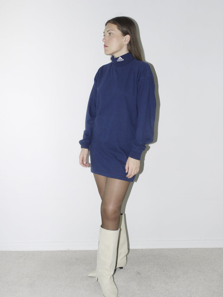 Vintage navy blue Adidas long-sleeve turtleneck top worn as a mini dress, styled with sheer tights and cream pointed boots – bold sportswear meets feminine edge.