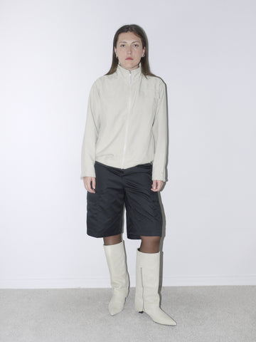 eutral-toned vintage Nike zip-up jacket with stand collar, paired with black satin bermuda cargo shorts and off-white pointed boots – sporty minimalism meets sleek streetwear.