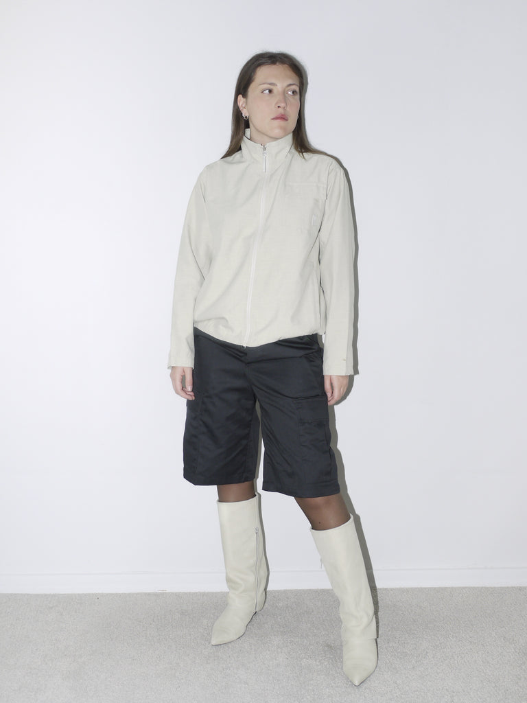 eutral-toned vintage Nike zip-up jacket with stand collar, paired with black satin bermuda cargo shorts and off-white pointed boots – sporty minimalism meets sleek streetwear.
