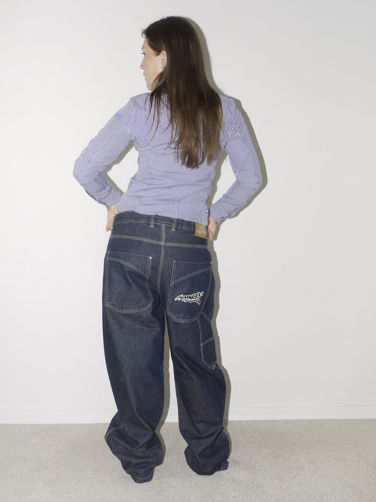 Slim-fit zip-up shirt in micro-gingham check paired with dark blue oversized denim jeans and pointed black shoes – a structured-meets-slouchy silhouette inspired by early 2000s streetwear.