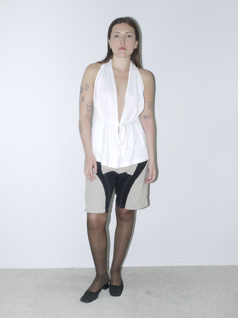 Vintage Diesel halter top in crisp white with deep plunge neckline and waist tie, styled with two-tone tech shorts and kitten heels for a bold Y2K-inspired look.