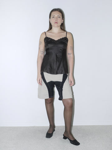 Vintage black satin cami with lace trim and delicate straps, styled with beige and black tech-panel shorts and classic black heels — sleek and subtly edgy.
