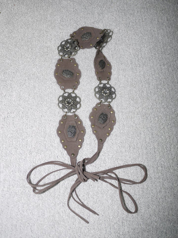 Vintage-inspired belt featuring taupe suede-like panels, antique silver floral medallions, and brass rivets. Adjustable tie closure.