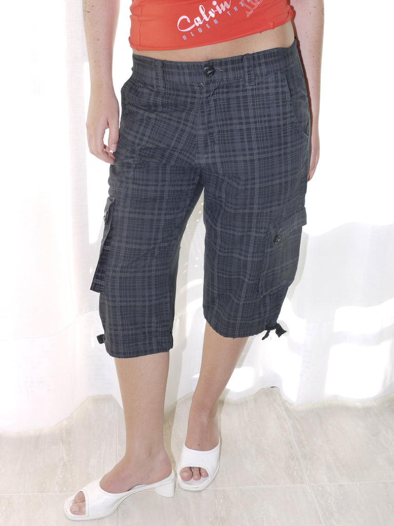 Model wearing a fitted red tank top with subtle graphic detailing, paired with low-rise dark capri pants featuring a checkered pattern and drawstring hems. Styled with black-and-white printed slingback heels, creating a sharp Y2K-inspired contrast. Shot against a plain white wall.