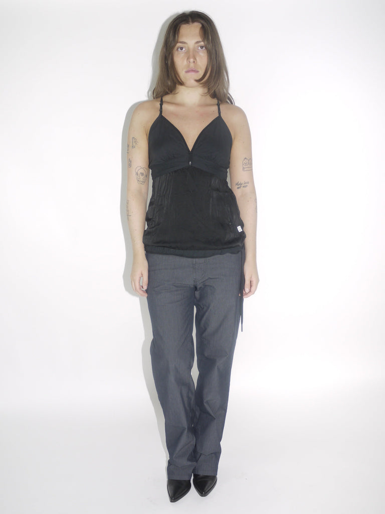 Model wearing a black G-Star halter top with a deep V-neckline and adjustable tie at the waist, paired with dark straight-leg trousers and pointed black boots. A sleek Y2K-inspired evening look with utilitarian undertones