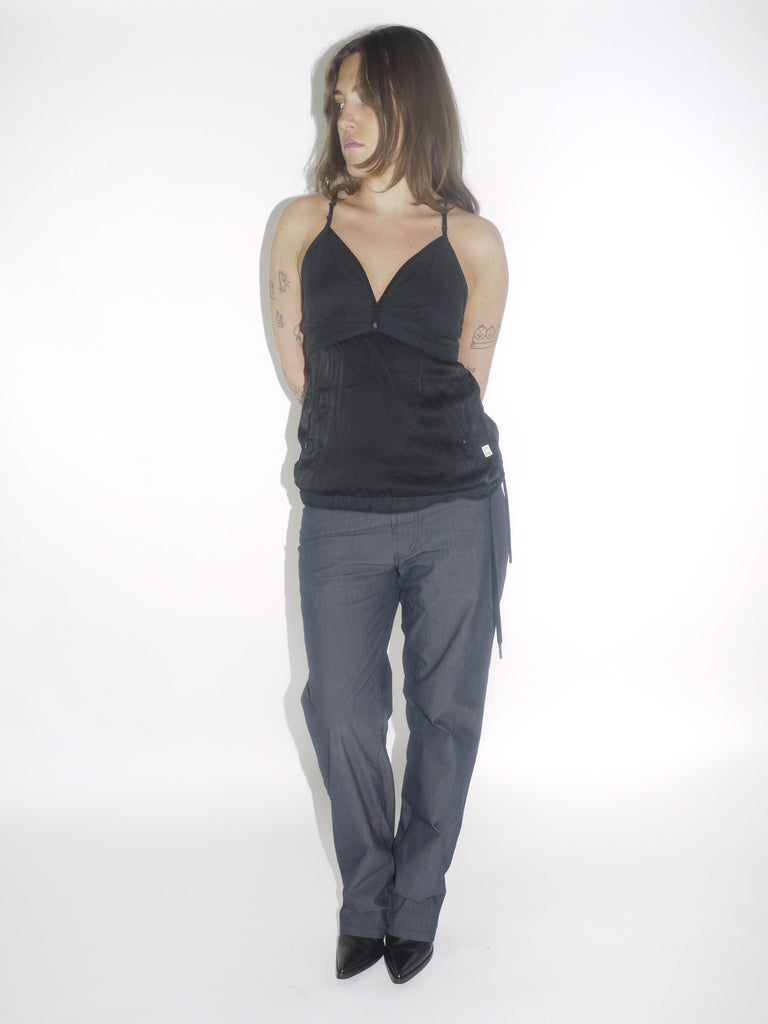 Model wearing a black G-Star halter top with a deep V-neckline and adjustable tie at the waist, paired with dark straight-leg trousers and pointed black boots. A sleek Y2K-inspired evening look with utilitarian undertones