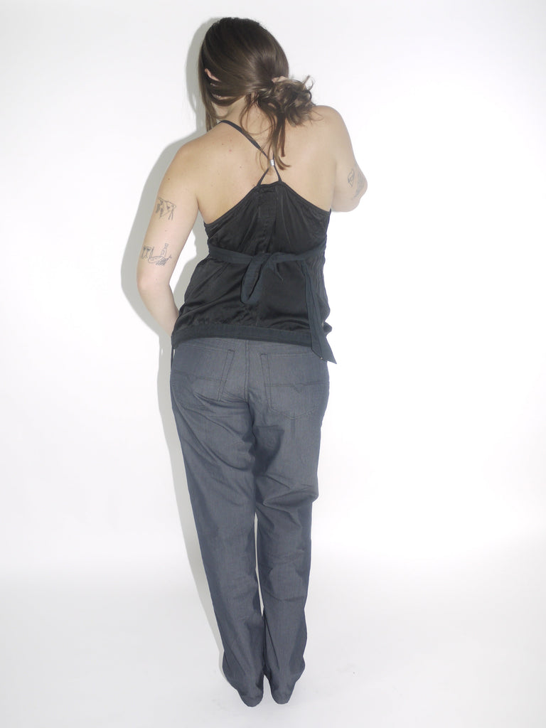 Model wearing a black G-Star halter top with a deep V-neckline and adjustable tie at the waist, paired with dark straight-leg trousers and pointed black boots. A sleek Y2K-inspired evening look with utilitarian undertones