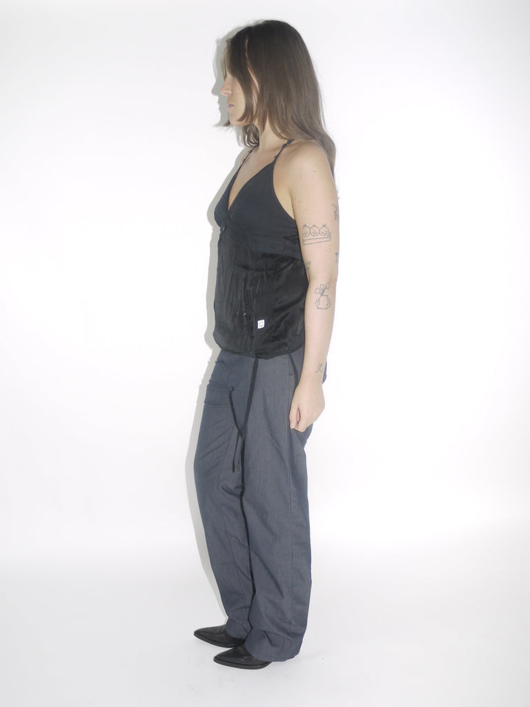 Model wearing a black G-Star halter top with a deep V-neckline and adjustable tie at the waist, paired with dark straight-leg trousers and pointed black boots. A sleek Y2K-inspired evening look with utilitarian undertones