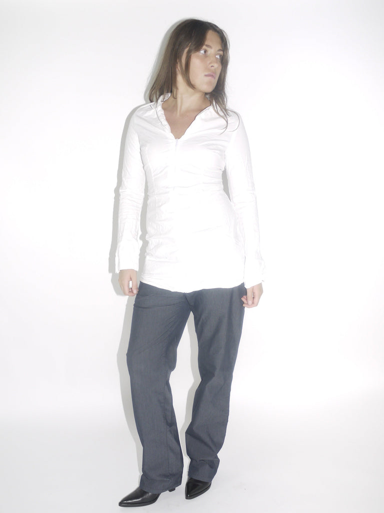 Model wearing a fitted white vintage shirt with a front zipper and ruched detailing, paired with straight-cut dark denim trousers and pointed black boots. A minimal yet structured early-2000s inspired look.