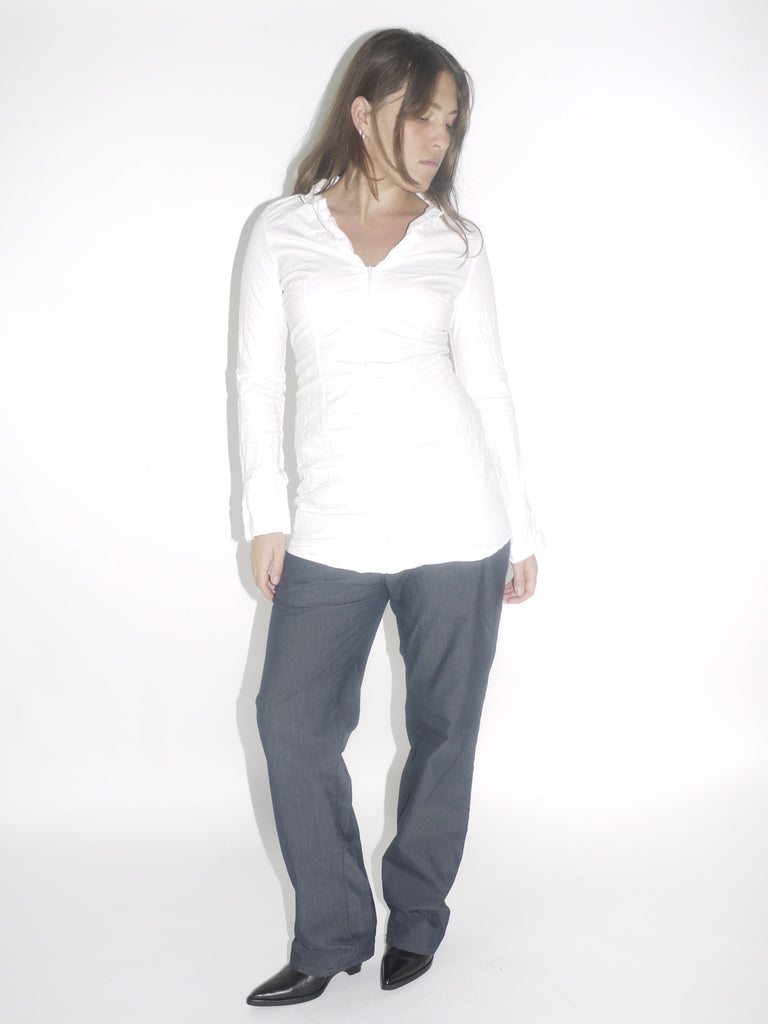 Model wearing a fitted white vintage shirt with a front zipper and ruched detailing, paired with straight-cut dark denim trousers and pointed black boots. A minimal yet structured early-2000s inspired look.