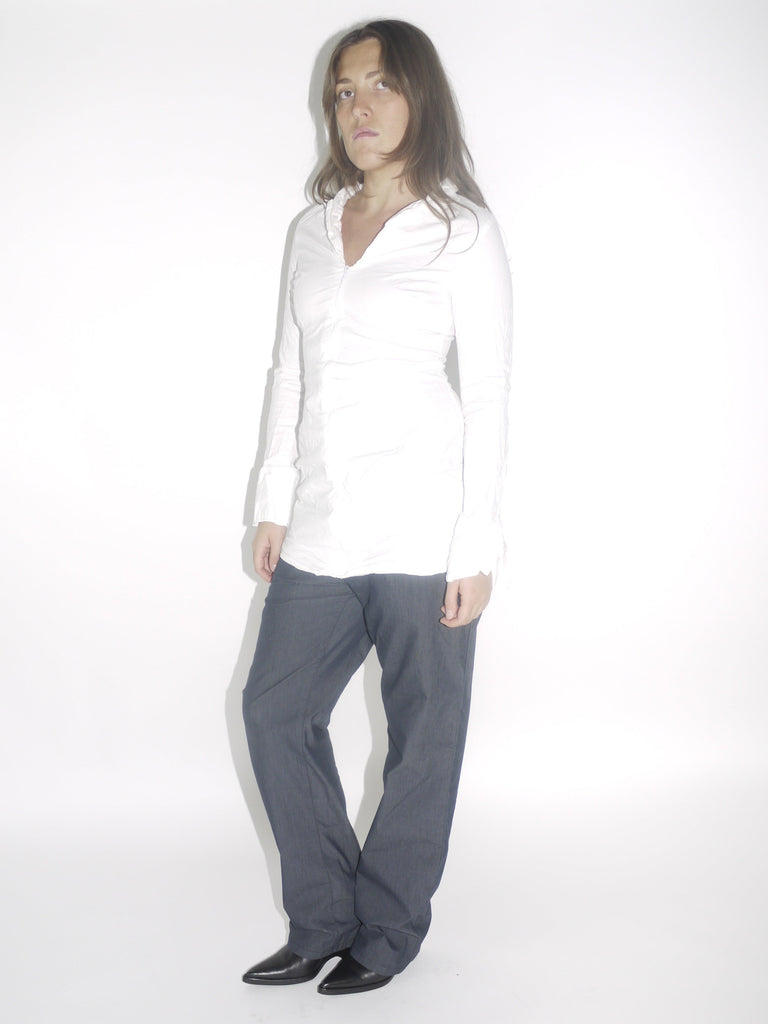 Model wearing a fitted white vintage shirt with a front zipper and ruched detailing, paired with straight-cut dark denim trousers and pointed black boots. A minimal yet structured early-2000s inspired look.