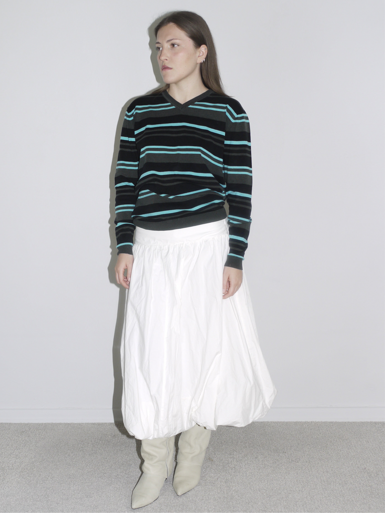 Model wearing a black long sleeve with mint and blue horizontal stripes, tucked into a voluminous white balloon skirt and styled with off-white cowboy boots. A laid-back vintage look blending skater Y2K with Cocaletto’s signature softness.