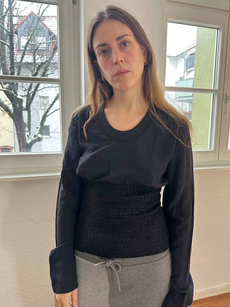 Avant-garde black long sleeve top with layered textures, inspired by Dries Van Noten’s signature deconstructed aesthetic, styled with grey Y2K print skirt, worn by model in natural light.