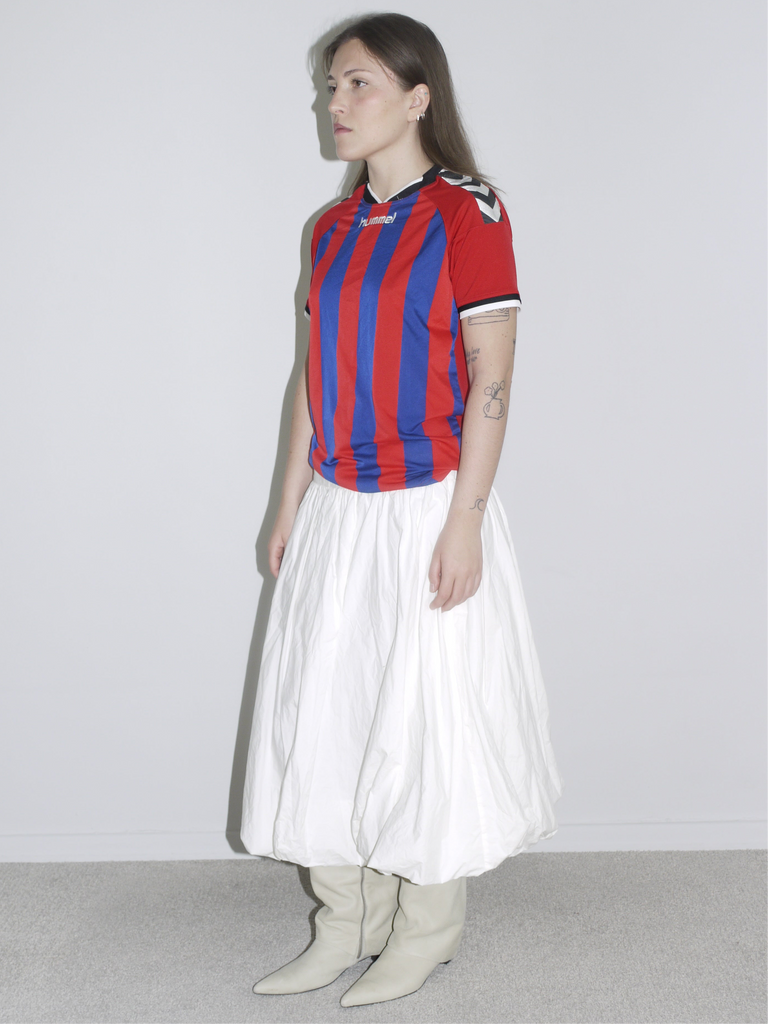 Vintage Hummel football jersey in red and blue stripes paired with a full white skirt and cream boots — sporty clash with vintage femininity.”