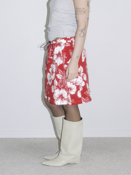 Side view of a red and white hibiscus print drawstring skirt styled with a grey tank top and off-white cowboy boots. Vintage surf aesthetic meets Y2K Western twist — think early 2000s beachcore with a fashion edge.