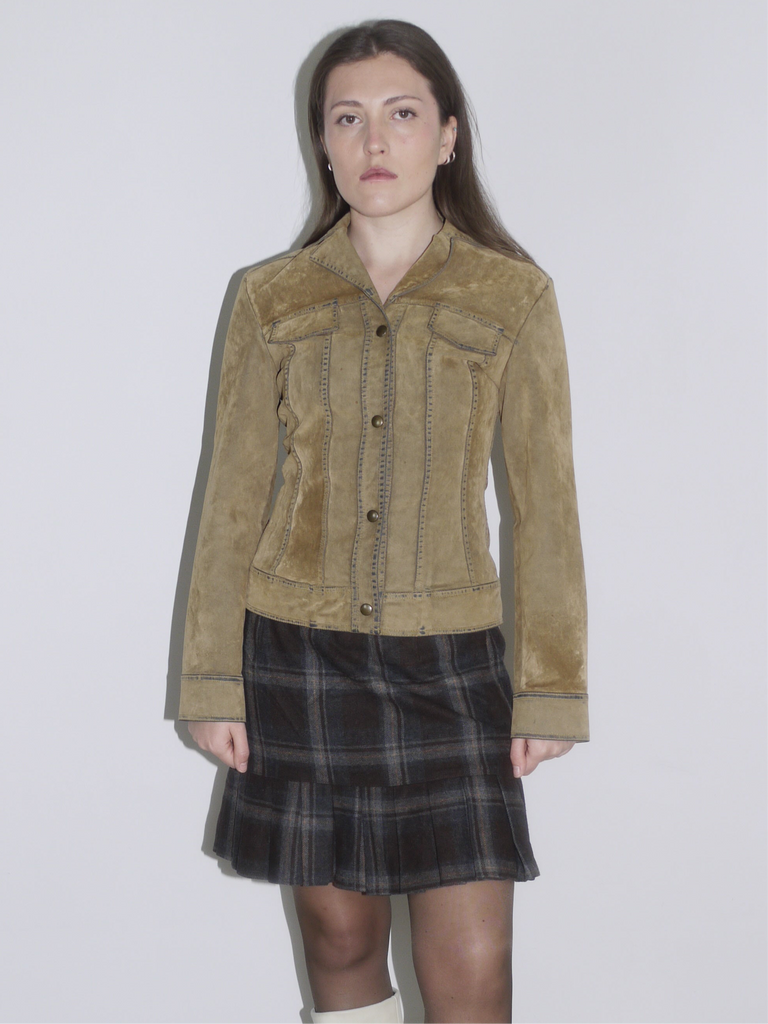 Woman wearing a structured camel suede jacket with contrast stitching, paired with a dark plaid mini skirt