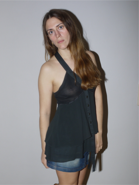 Original Cop Copine asymmetrical black tunic top with halter neckline and layered sheer panel, Y2K-inspired designer piece styled with mini skirt and boots, modeled indoors.

