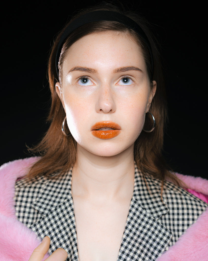 Model wearing an oversized checkered blazer paired with wide brown trousers – bold look with bright orange lipstick and pink faux fur detail, inspired by Maison Margiela and 90s editorials.