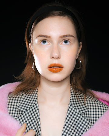 Model wearing an oversized checkered blazer paired with wide brown trousers – bold look with bright orange lipstick and pink faux fur detail, inspired by Maison Margiela and 90s editorials.