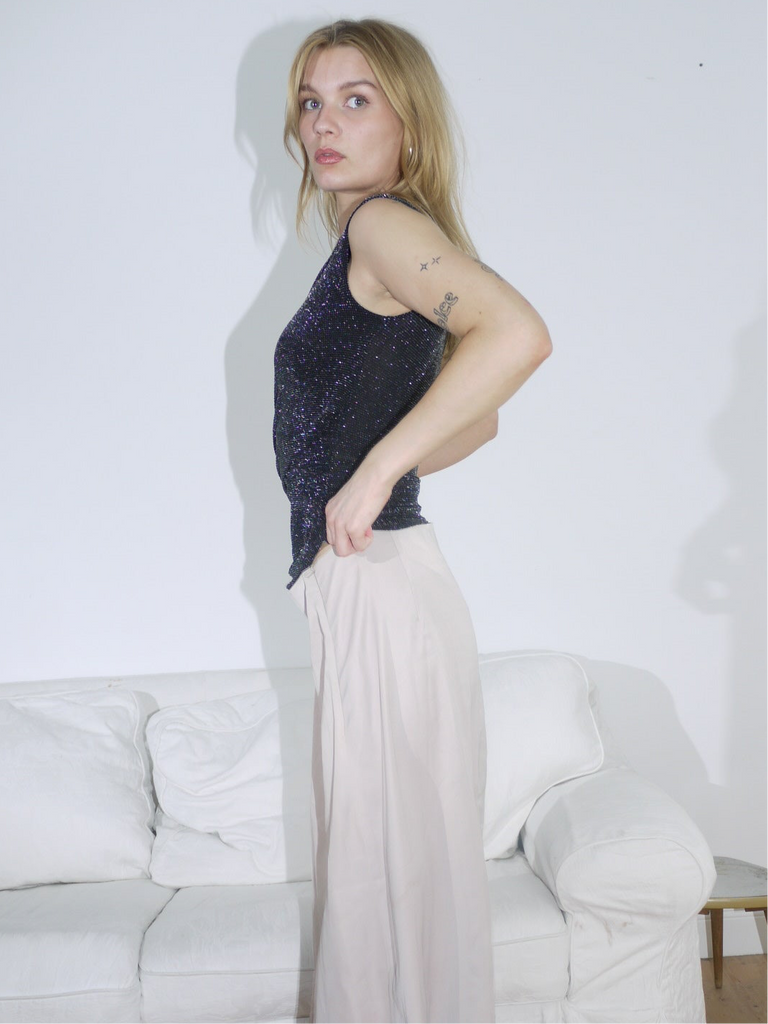 Model styled in a sparkly black sleeveless top paired with a flowy beige maxi skirt. The look balances soft movement with evening glam — perfect for summer dinners or low-key parties.
