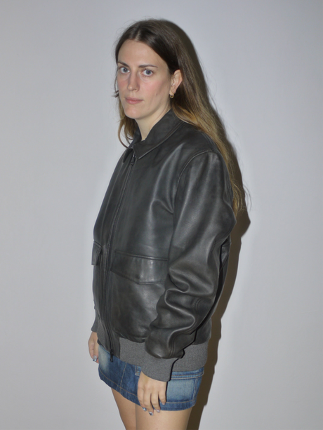 Original Marc O’Polo black leather bomber jacket with ribbed cuffs and waistband, zip front and relaxed fit, styled with denim mini skirt, modeled against plain background.