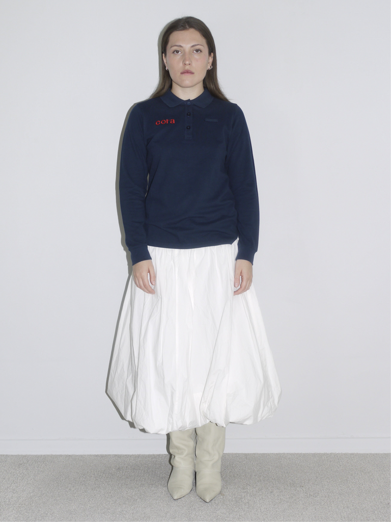 Back view of a navy blue French logo sweatshirt reading “Cora – Comptez sur nous,” styled with a voluminous white balloon skirt and pointed cream boots. A casual meets editorial streetwear look with vintage flair.