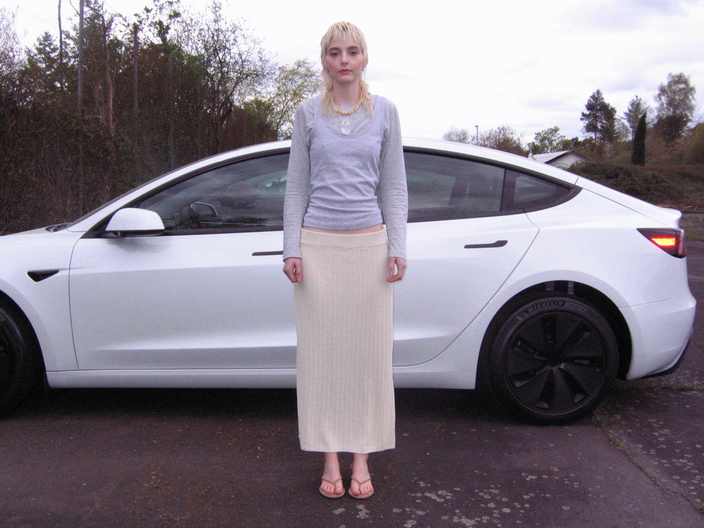 Model wearing a cream ribbed maxi skirt and light grey long sleeve top standing in front of a white car – styled and curated by Cocaletto, your destination for selected vintage fashion online.