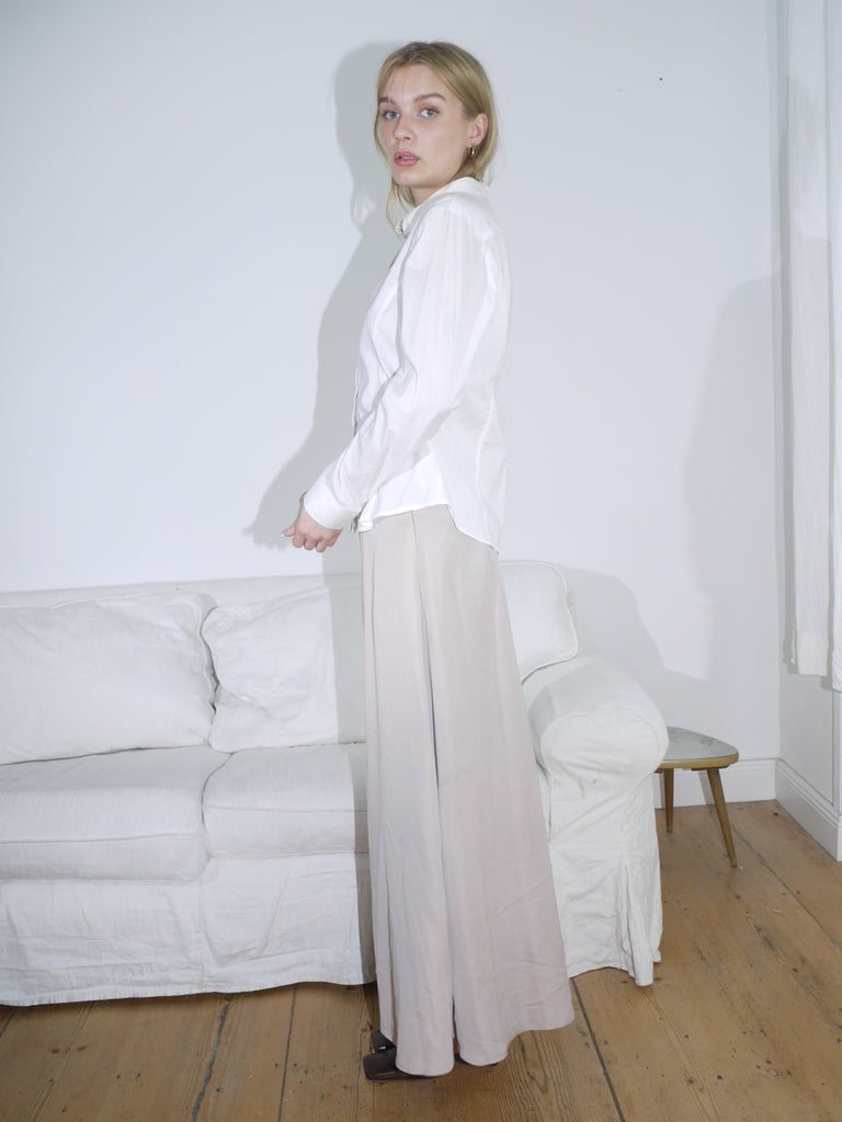 Model wearing a soft beige low-rise maxi skirt with a fluid, slightly flared silhouette. Styled with a cropped black top and cream leather mules for an understated, modern look.