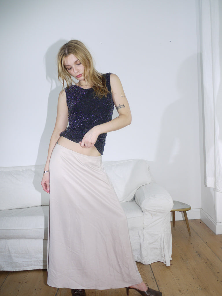 Model styled in a sparkly black sleeveless top paired with a flowy beige maxi skirt. The look balances soft movement with evening glam — perfect for summer dinners or low-key parties.