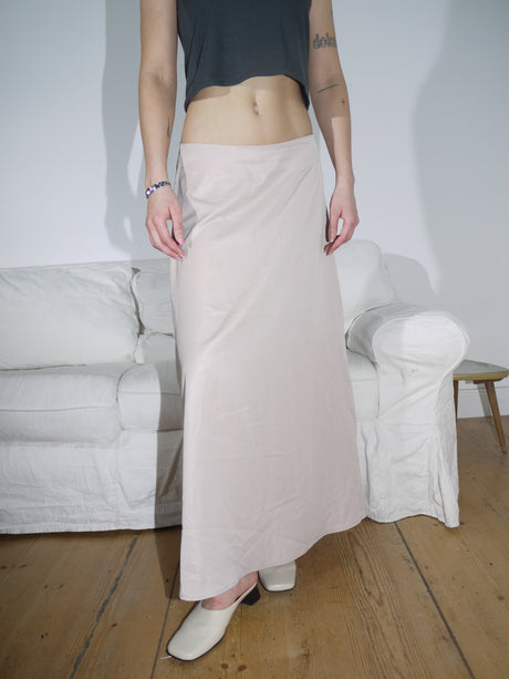 Model wearing a soft beige low-rise maxi skirt with a fluid, slightly flared silhouette. Styled with a cropped black top and cream leather mules for an understated, modern look.