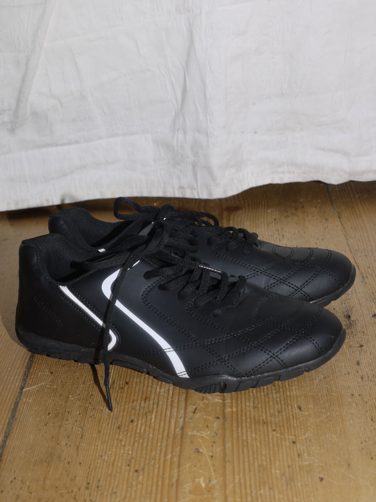 Black athletic-style sneakers with a glossy finish and white curved side detail, reminiscent of early 2000s streetwear aesthetics