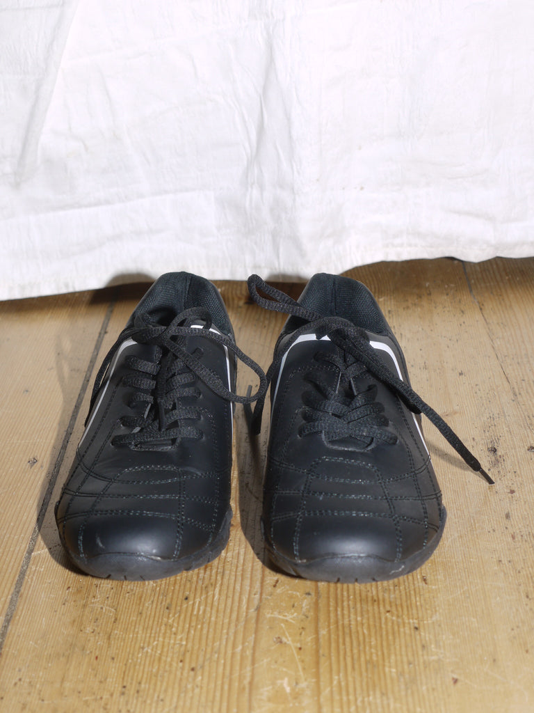 Black athletic-style sneakers with a glossy finish and white curved side detail, reminiscent of early 2000s streetwear aesthetics