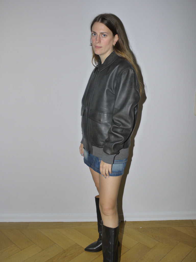 Original Marc O’Polo black leather bomber jacket with ribbed cuffs and waistband, zip front and relaxed fit, styled with denim mini skirt, modeled against plain background.
