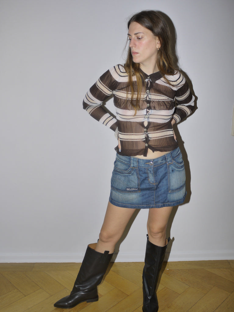 Original Jacquemus sheer mesh blouse with brown and cream horizontal stripes, button-down front and fitted silhouette, styled with denim mini skirt and boots, modeled indoors.