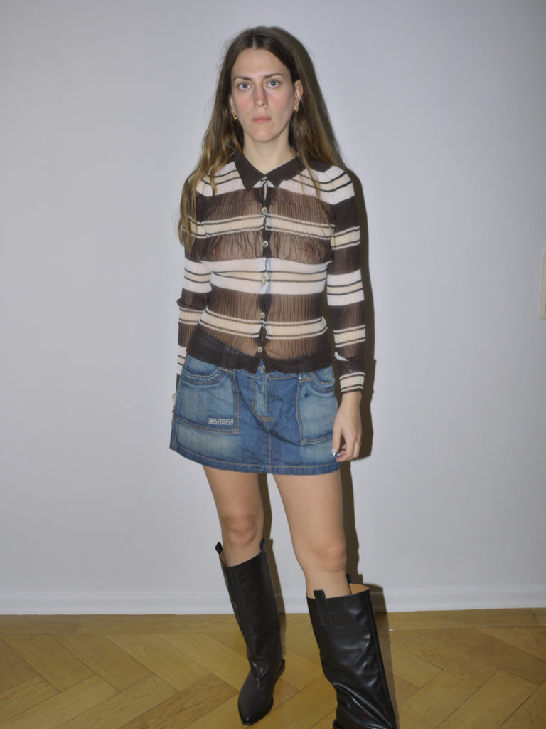 Original Jacquemus sheer mesh blouse with brown and cream horizontal stripes, button-down front and fitted silhouette, styled with denim mini skirt and boots, modeled indoors.
