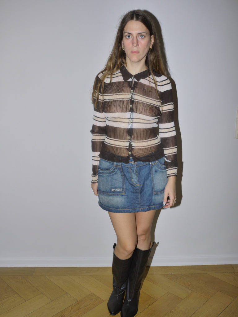 Original Jacquemus sheer mesh blouse with brown and cream horizontal stripes, button-down front and fitted silhouette, styled with denim mini skirt and boots, modeled indoors.